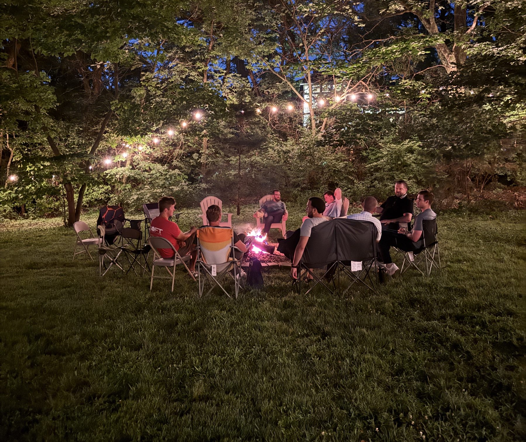 Men gathered in a circle around a fire under string lights