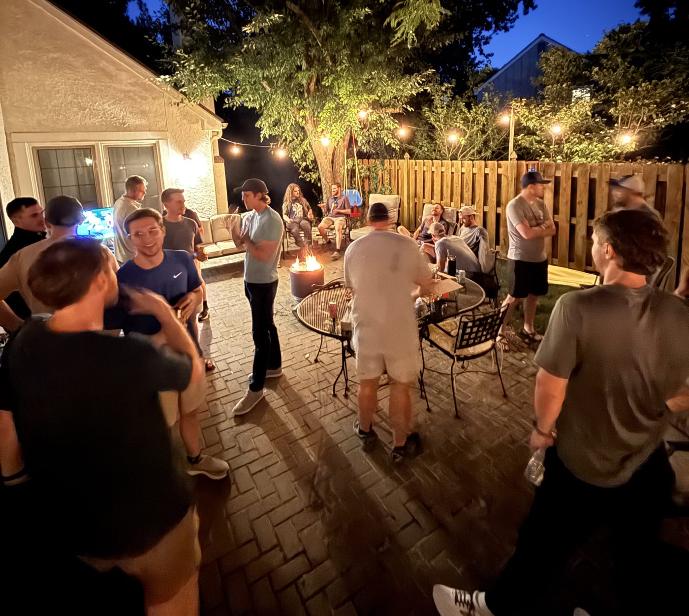 Men talking around a fire pit on a patio at night